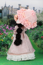 Vintage-style doll in a pink dress and bonnet with a castle and garden in the background
