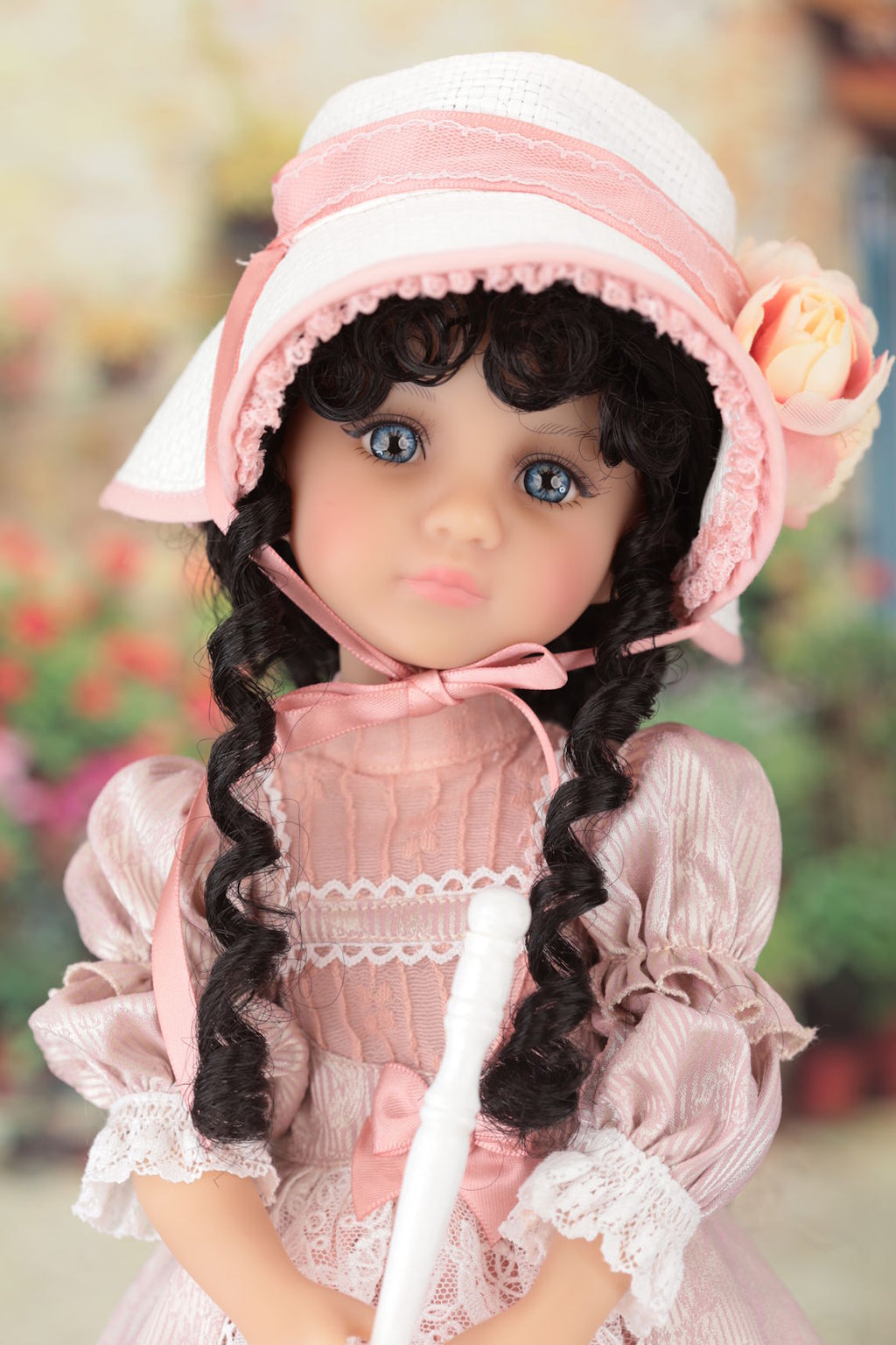 Doll with pink dress and hat against a blurred floral background