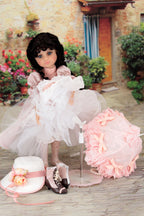 Doll in a white dress with accessories on a wooden floor outdoors.