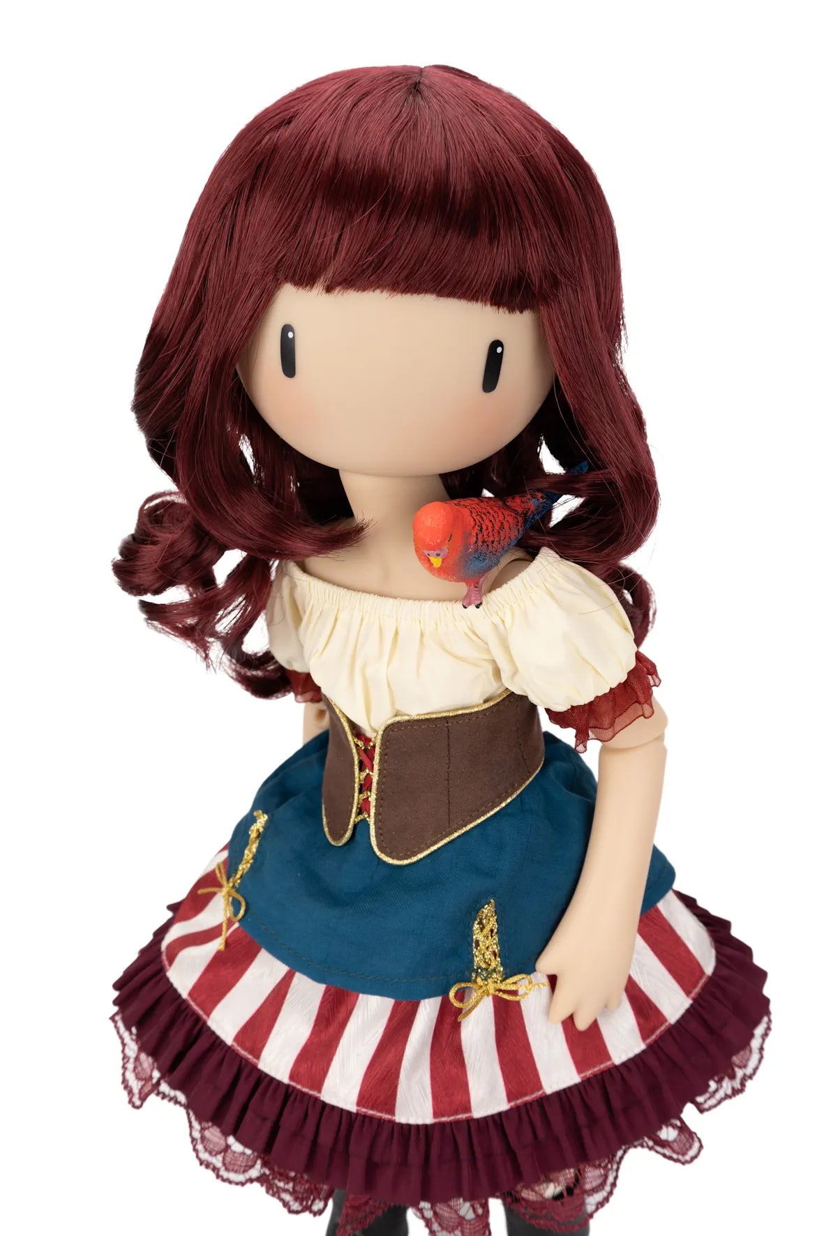 A stylized Gorjuss doll with long burgundy hair, a cream ruffled bodice, a blue skirt panel, red-and-white striped skirt, and a small red-and-blue bird on her shoulder, shown against a plain white background.
