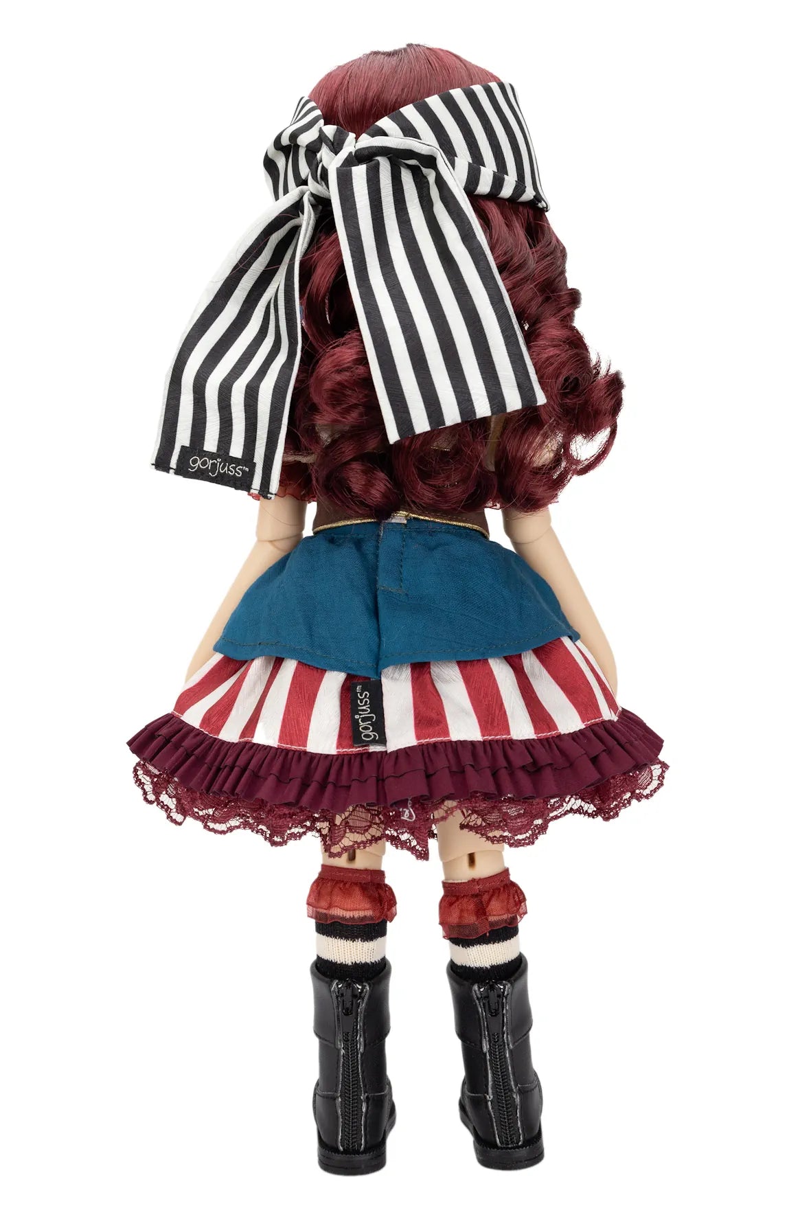 Back view of a Gorjuss doll with long wavy burgundy hair, wearing a black and white striped bow headband, a blue denim-style top, a red, white, and blue striped skirt with lace trim, red-and-white striped socks, and black boots on a white background.