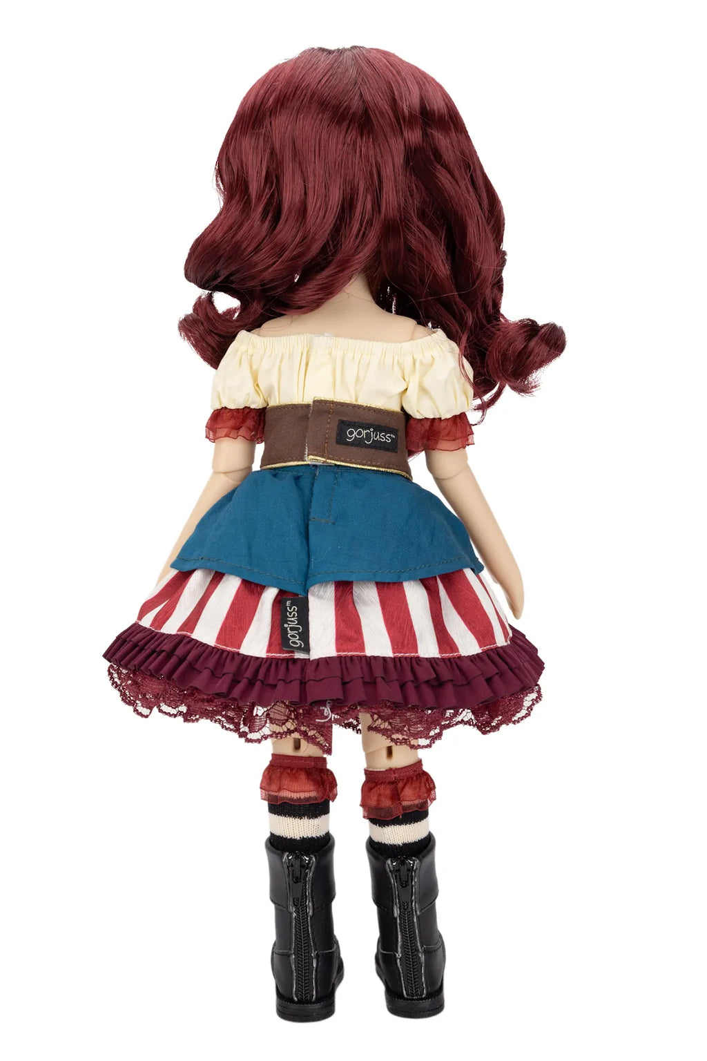A Gorjuss doll viewed from the back, featuring long wavy burgundy hair, a cream off-the-shoulder top, a blue waist section, a red and white striped skirt with a burgundy lace hem, red cuffs, and black boots, set against a plain white background.