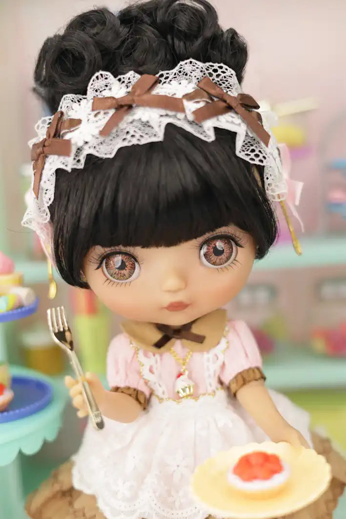 Mori Lolli Doll with black hair styled in pigtails, wearing a white lace headband and holding a plate with a dessert.