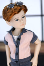 Doll with sunglasses on head wearing a pink shirt and dark pants.