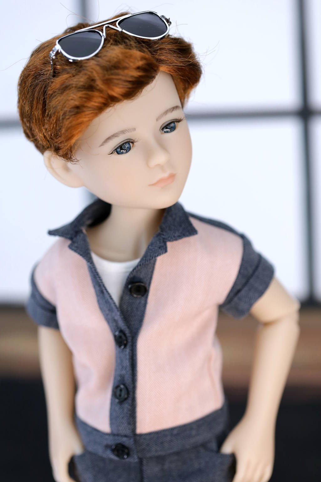 Doll with sunglasses on head wearing a pink shirt and dark pants.
