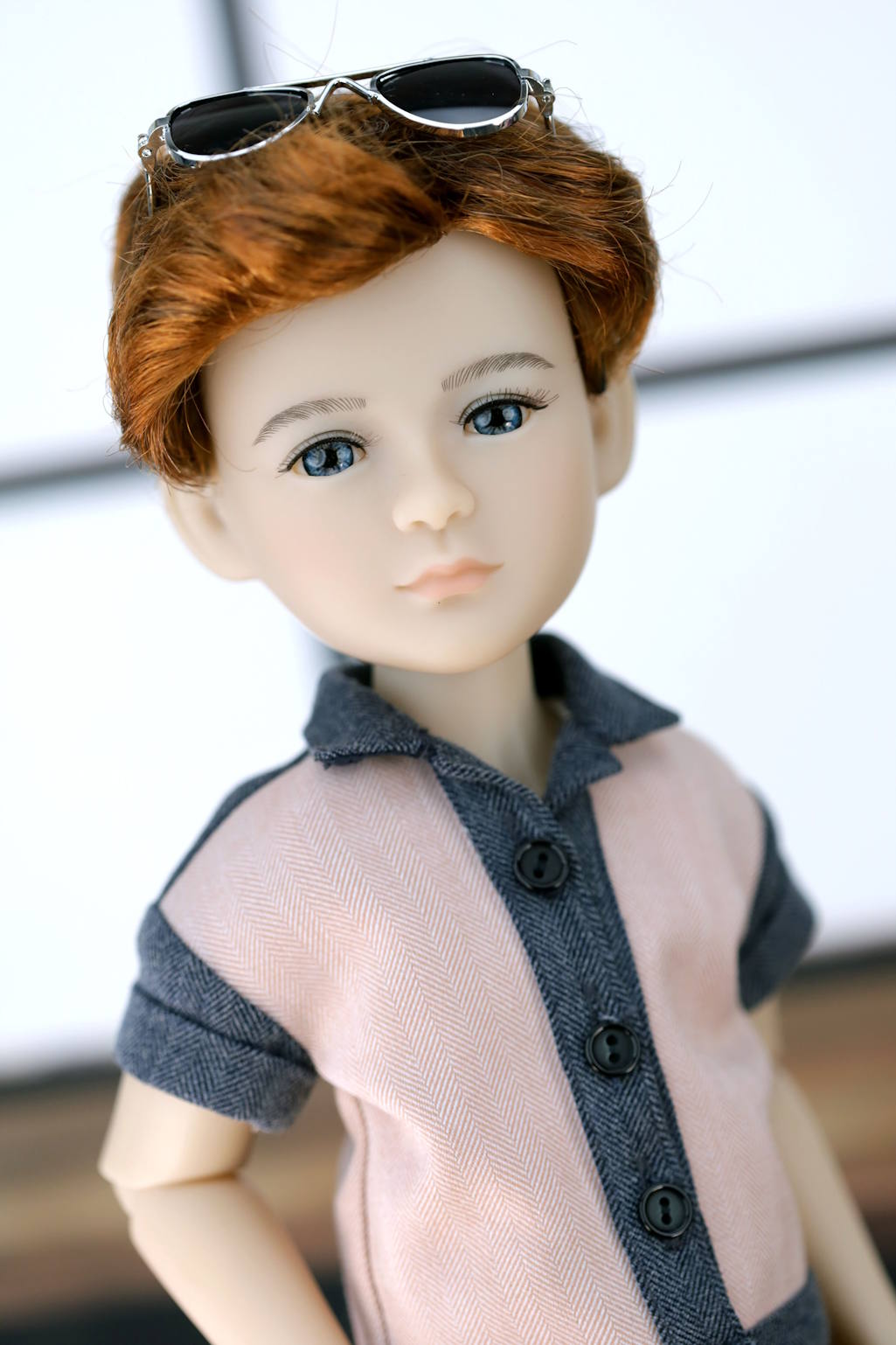 Doll with red hair and sunglasses on head, wearing a gray shirt with sheer overlay.