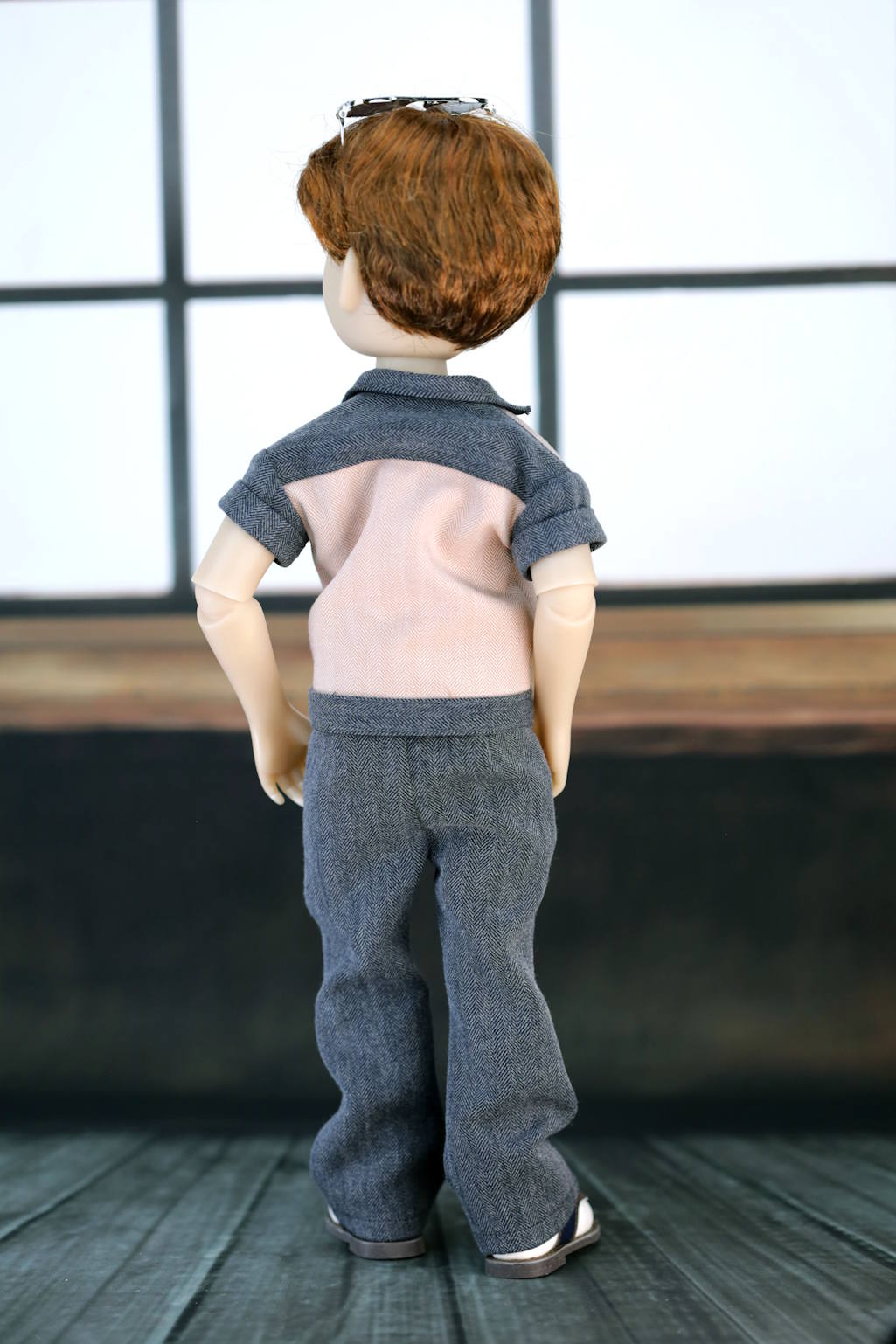 Doll wearing a gray shirt and pants with a blurred background