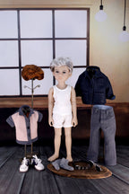 Doll with clothing items on a wooden floor in a room with large windows.