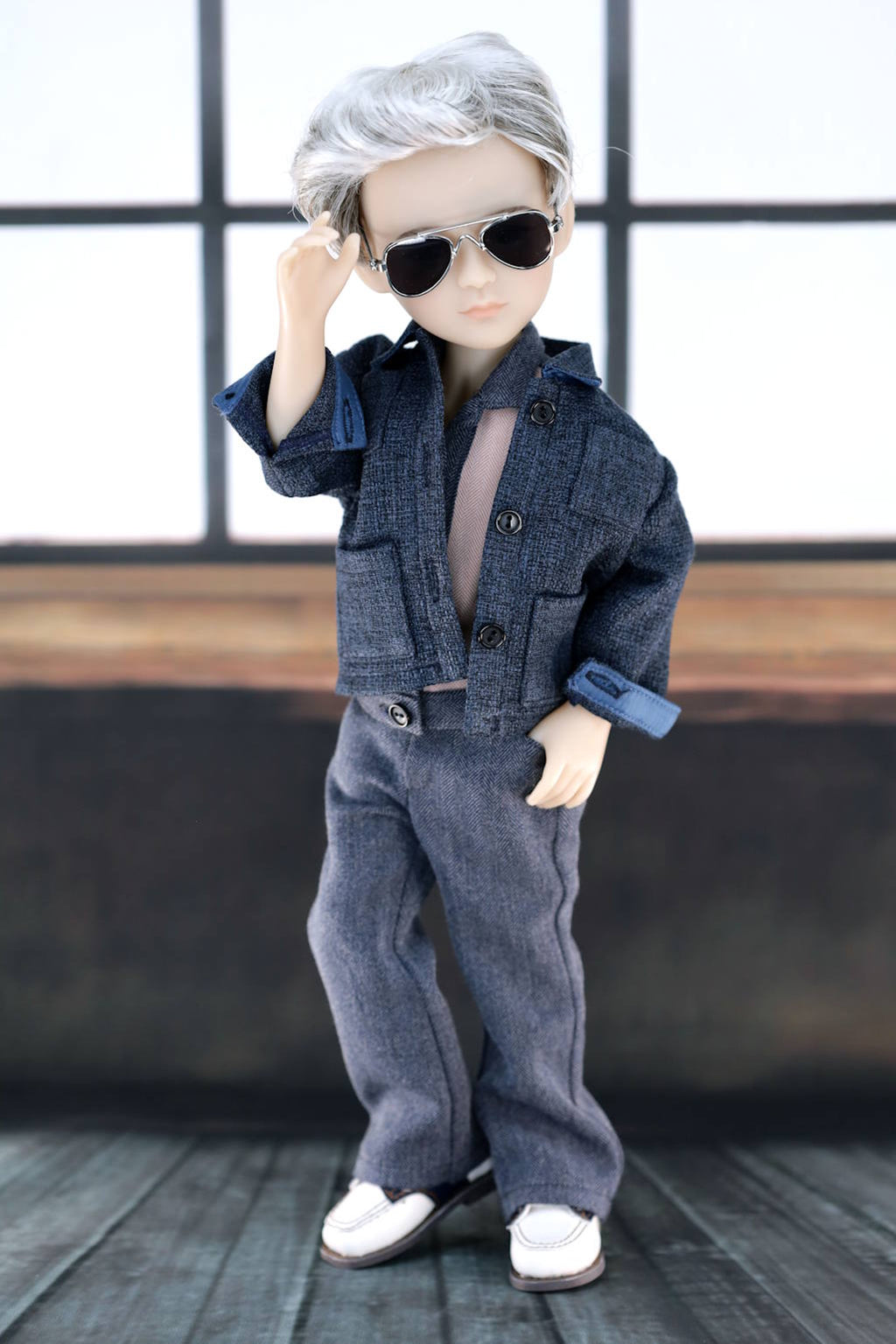 Doll wearing a denim outfit with sunglasses against a window background