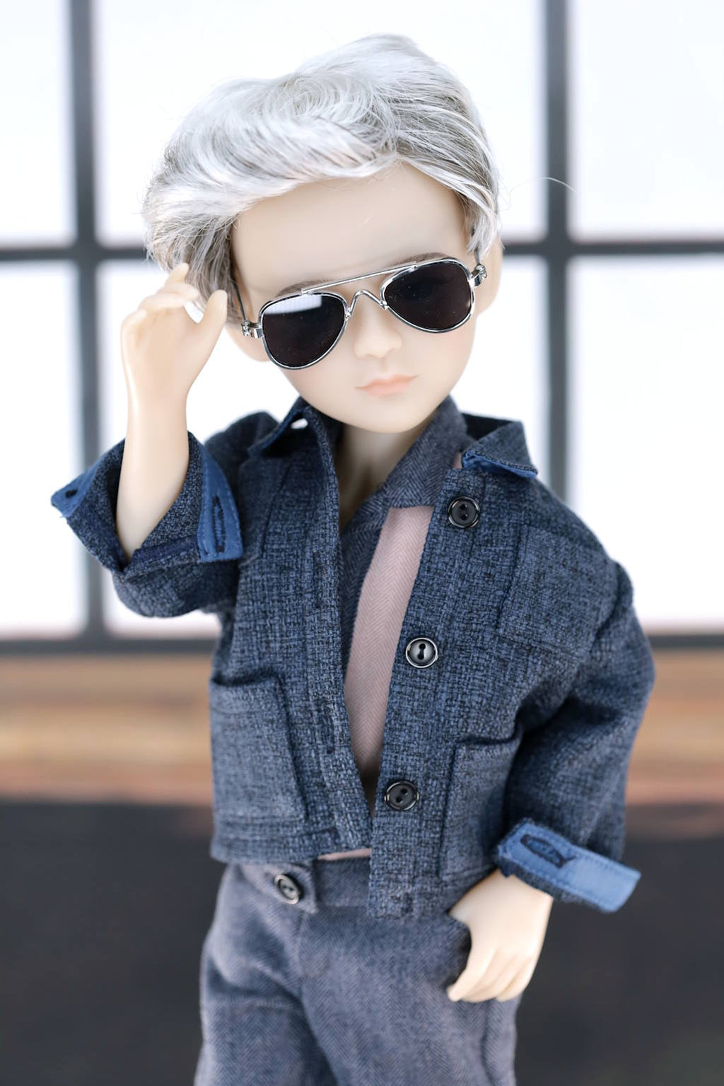 Doll wearing a blue jacket and sunglasses with a blurred background