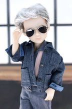 Doll wearing a blue jacket and sunglasses with a blurred background