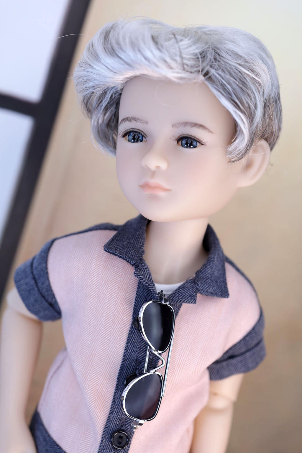Doll with gray hair wearing a shirt and sunglasses on a neutral background