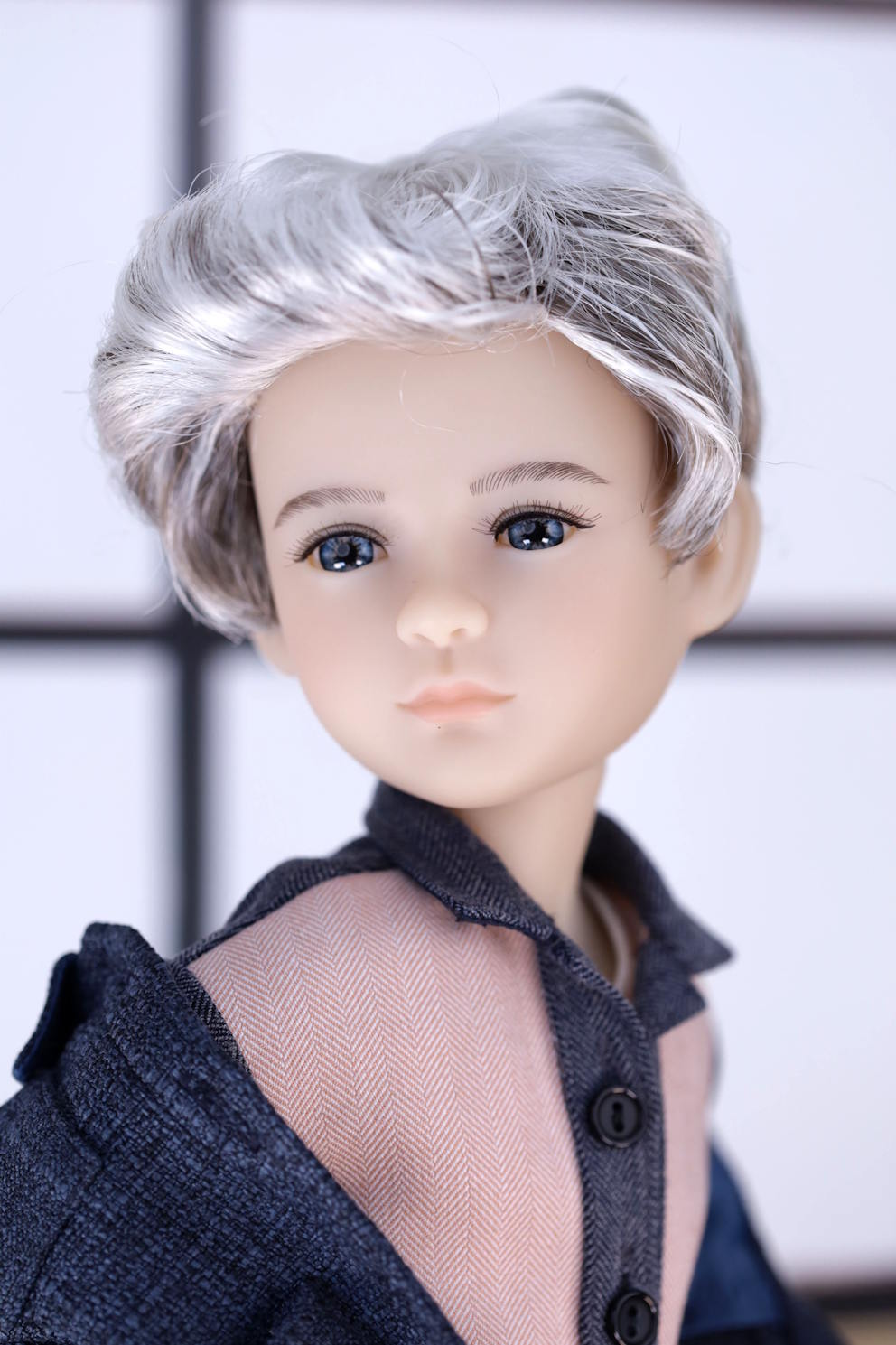 Close-up of a doll with gray hair and a dark outfit against a neutral background