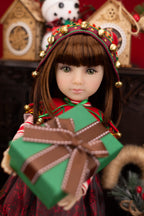 Doll wearing a festive outfit with a green gift box, surrounded by Christmas decorations.