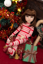 Doll in red and white striped pajamas sitting next to a Christmas tree and gift box.