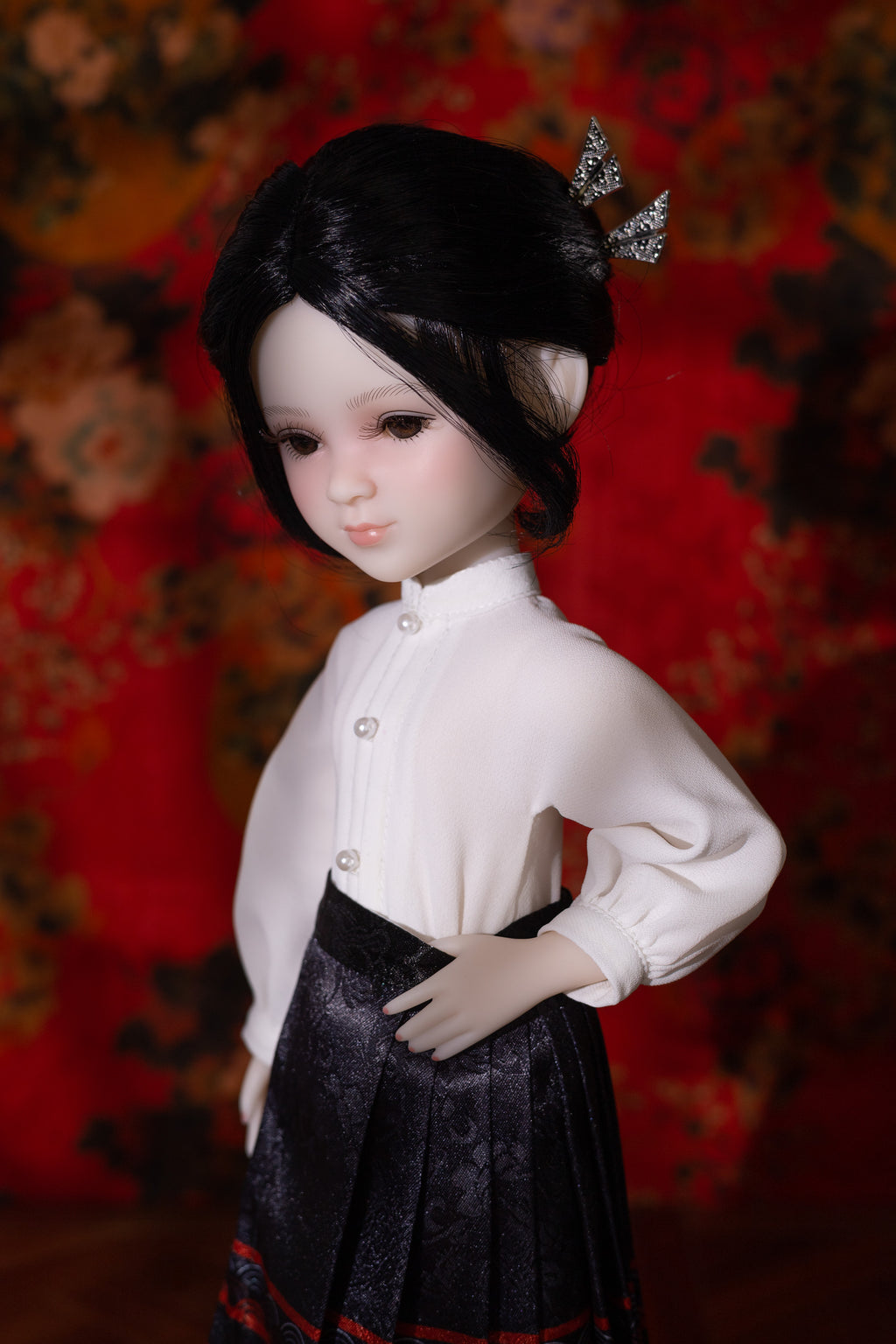 Doll wearing a white blouse and dark pleated skirt against a patterned background