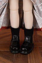 Doll wearing black shoes on a wooden floor.
