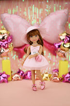 Doll in a pink dress and hat surrounded by festive decorations