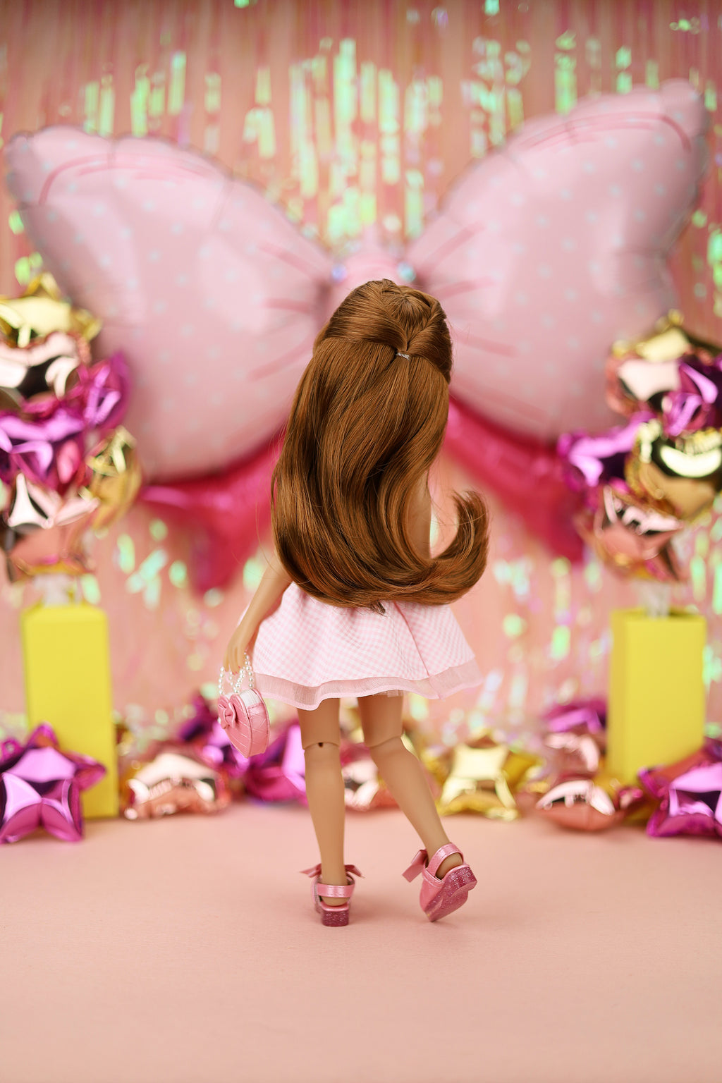 Doll in pink dress in front of colorful balloons and decorations