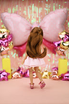 Doll in pink dress in front of colorful balloons and decorations
