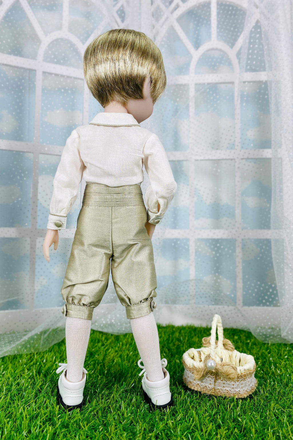 Doll in formal attire standing on grass with a basket, against a window pane background