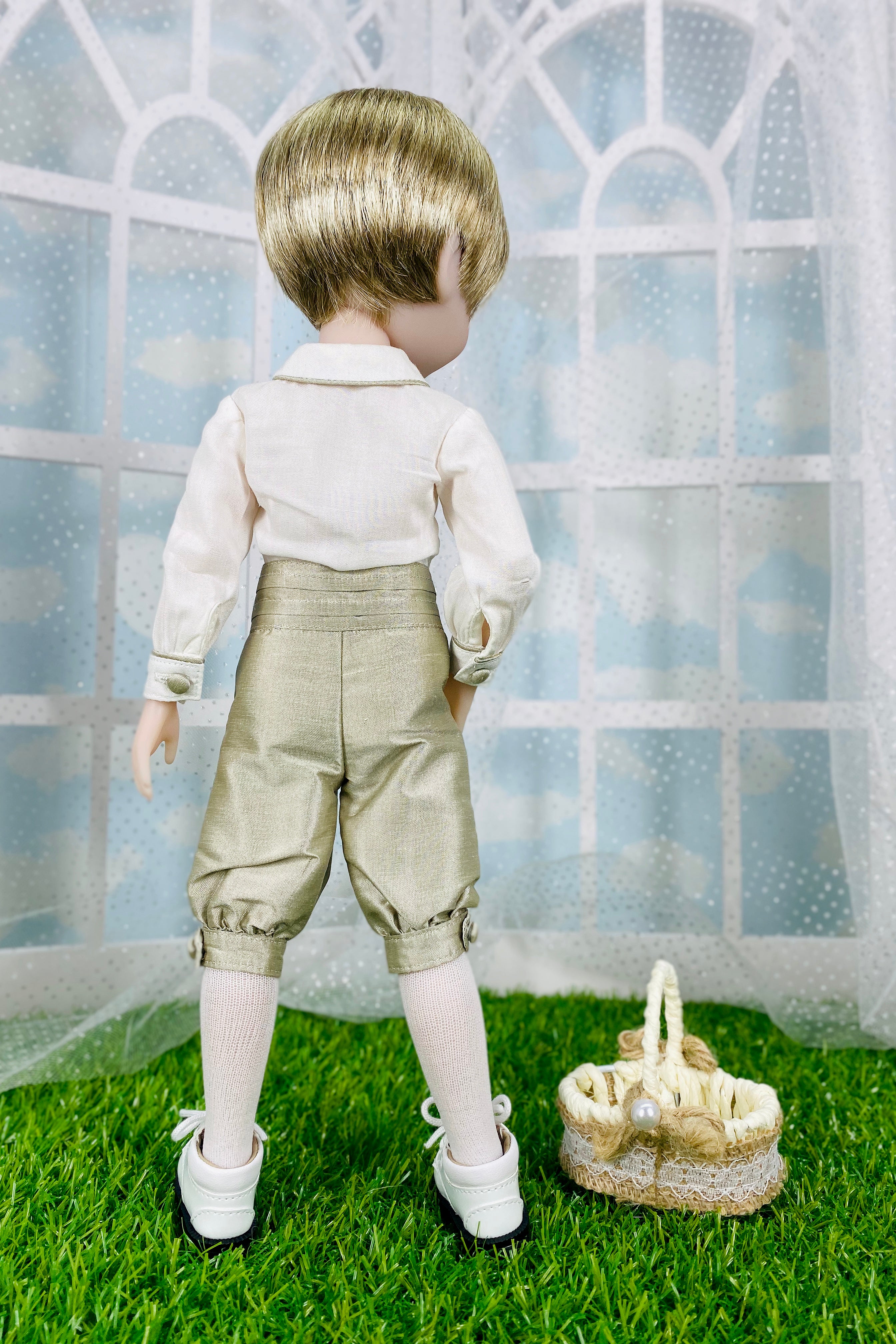 Doll in formal attire standing on grass with a basket, against a window pane background