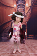 Doll in a vintage outfit with floral details standing in an elegant interior setting.