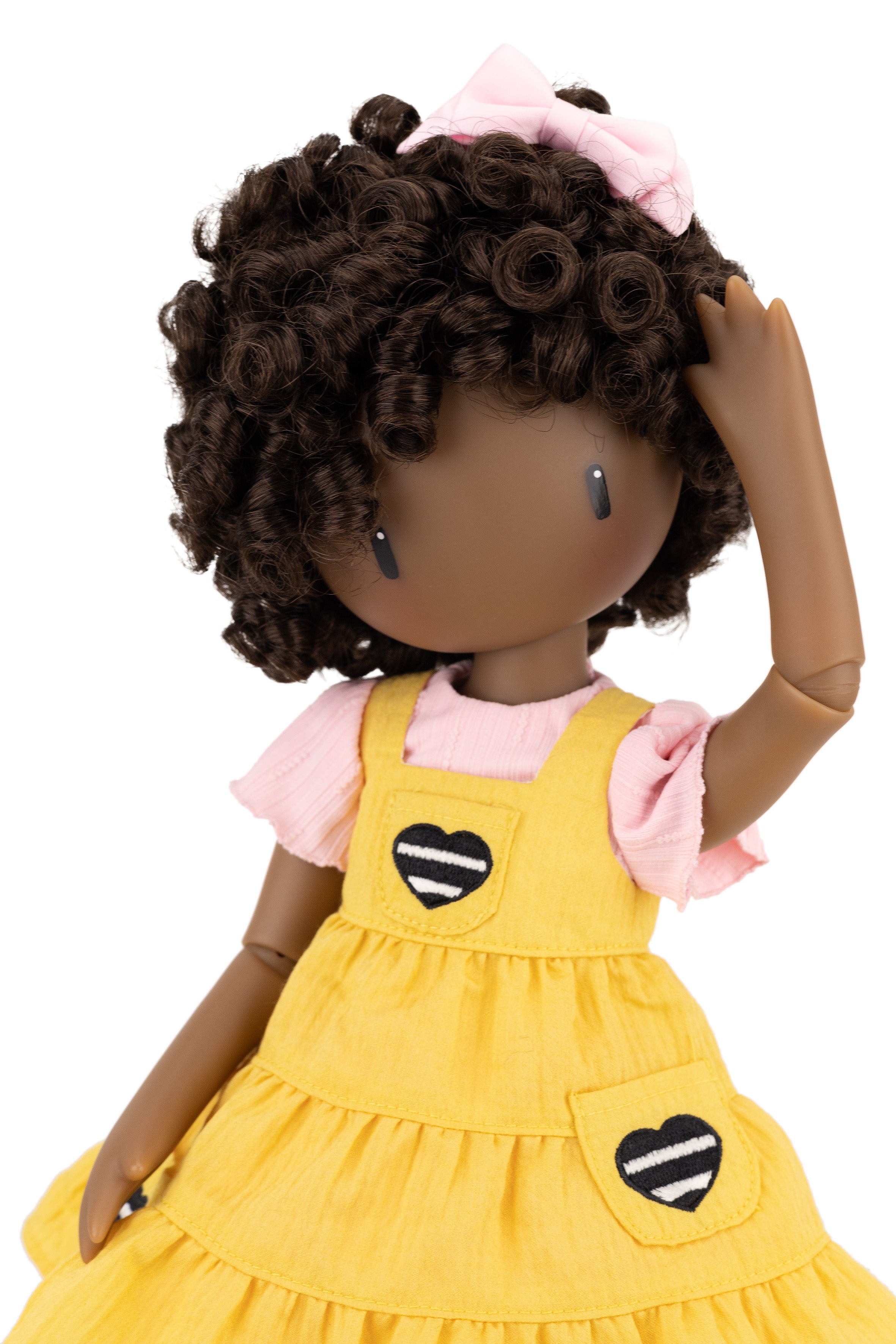 Doll with curly hair wearing a yellow dress with black and white heart patterns on a white background