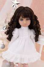 Doll with long brown hair wearing a white dress in a decorative setting.