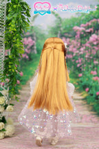 Doll with long blonde hair and a sparkly dress standing in a garden with pink flowers and greenery.
