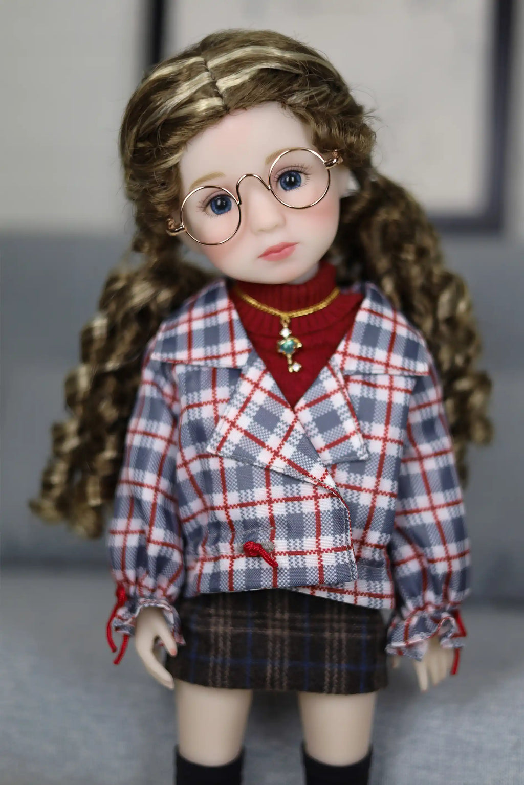 Doll wearing a plaid shirt and skirt with a red sweater underneath, on a neutral background.