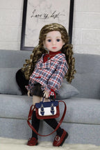 Doll wearing a plaid outfit with a handbag on a gray couch