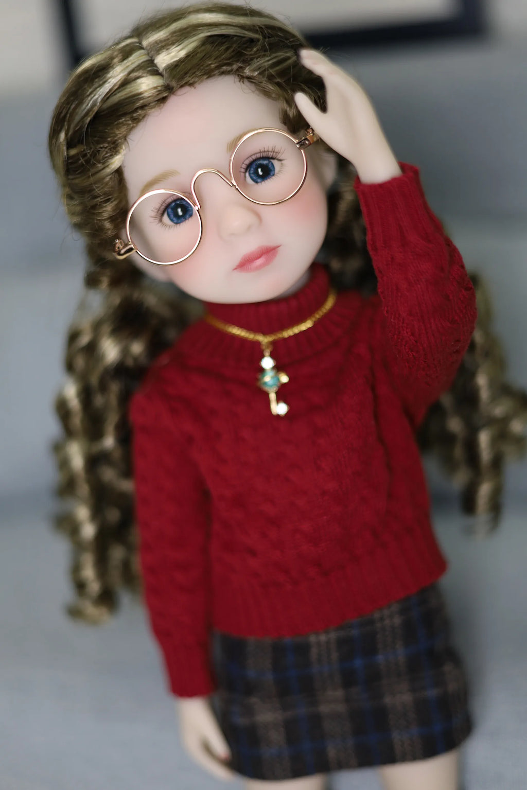 Doll wearing a red sweater and plaid skirt with a blurred background