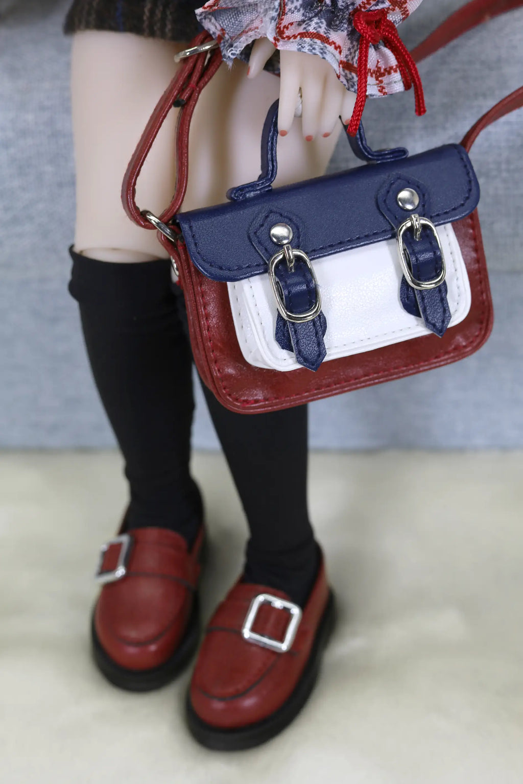 Small red and blue handbag held by a person wearing black shoes and socks.