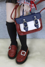 Small red and blue handbag held by a person wearing black shoes and socks.