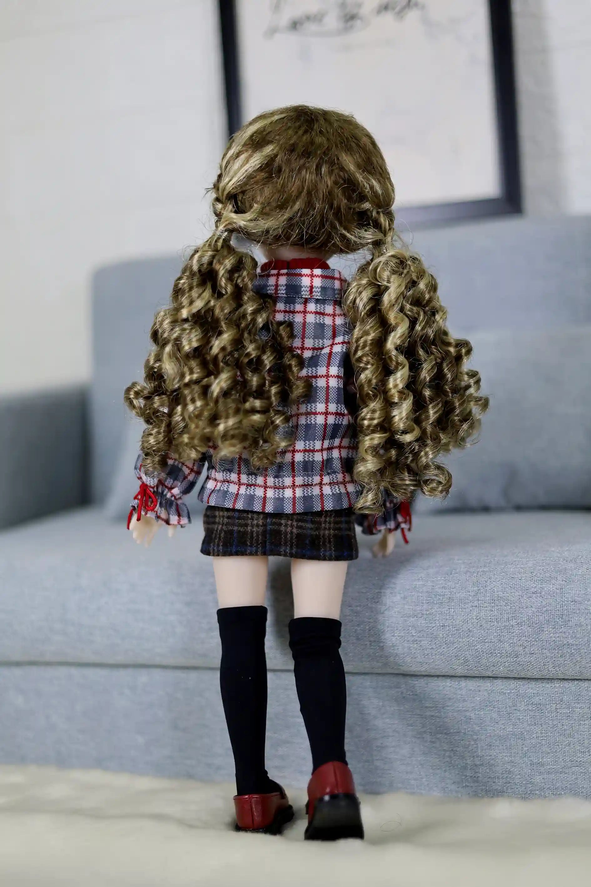 Back view of a doll with curly hair wearing a plaid shirt and skirt on a light blue couch.