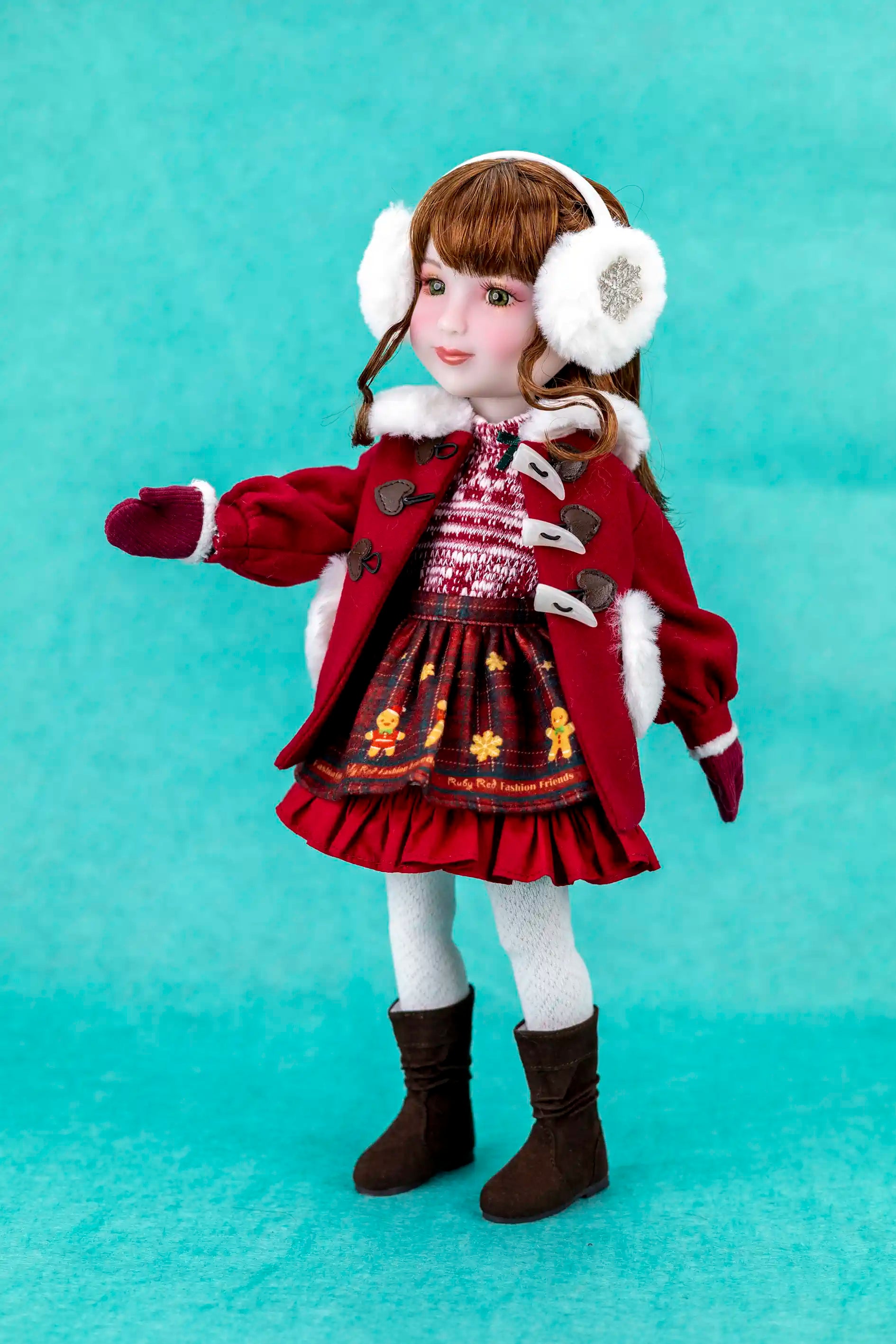 Doll wearing a red coat, dress, and white earmuffs on a teal background
