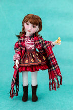 Doll wearing a red dress with plaid shawl on a teal background
