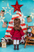 Doll in a red coat standing in front of a Christmas tree with decorations on a blue background
