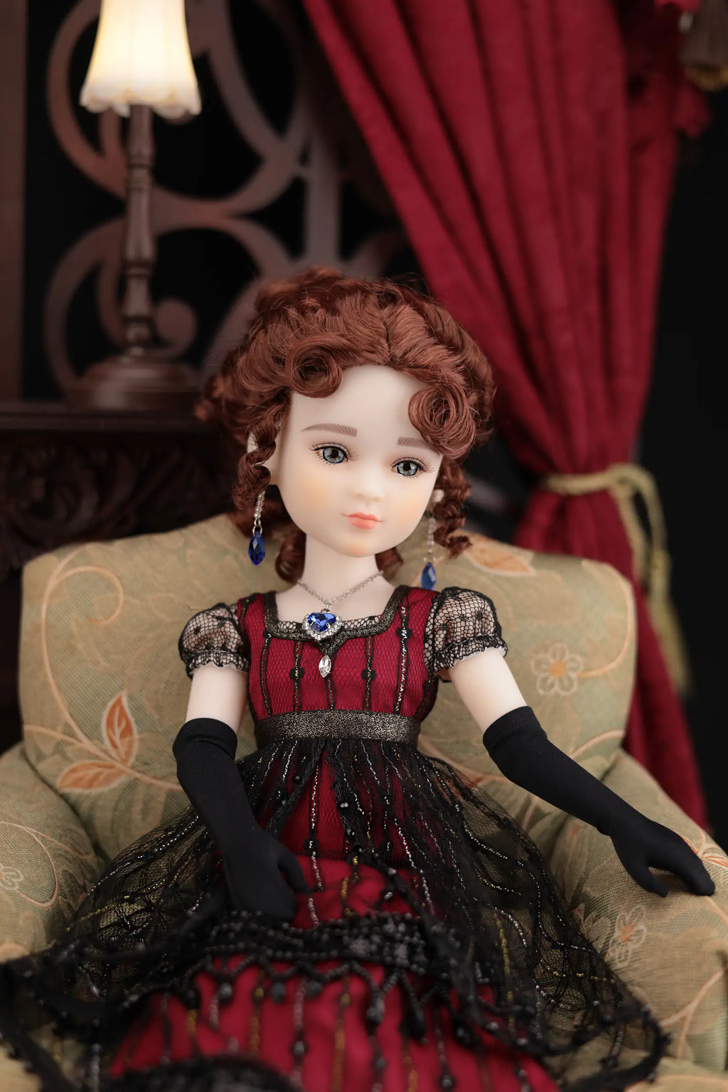 Doll with red hair and a red dress sitting on an ornate chair with a dark background