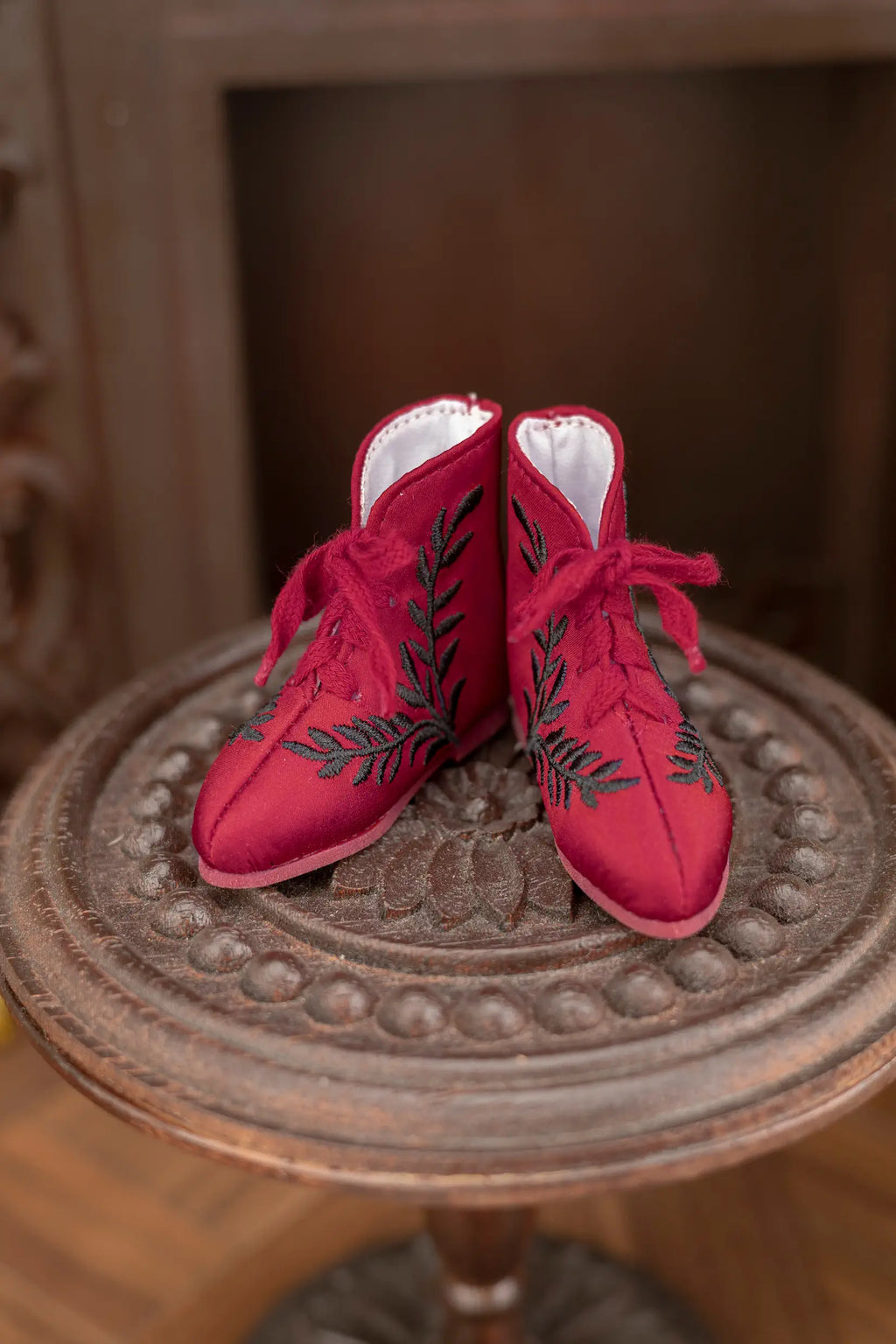 Pair of red shoes with black embroidery on a decorative wooden table.
