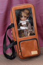Brown leather doll carrier with a doll inside, on a striped fabric background