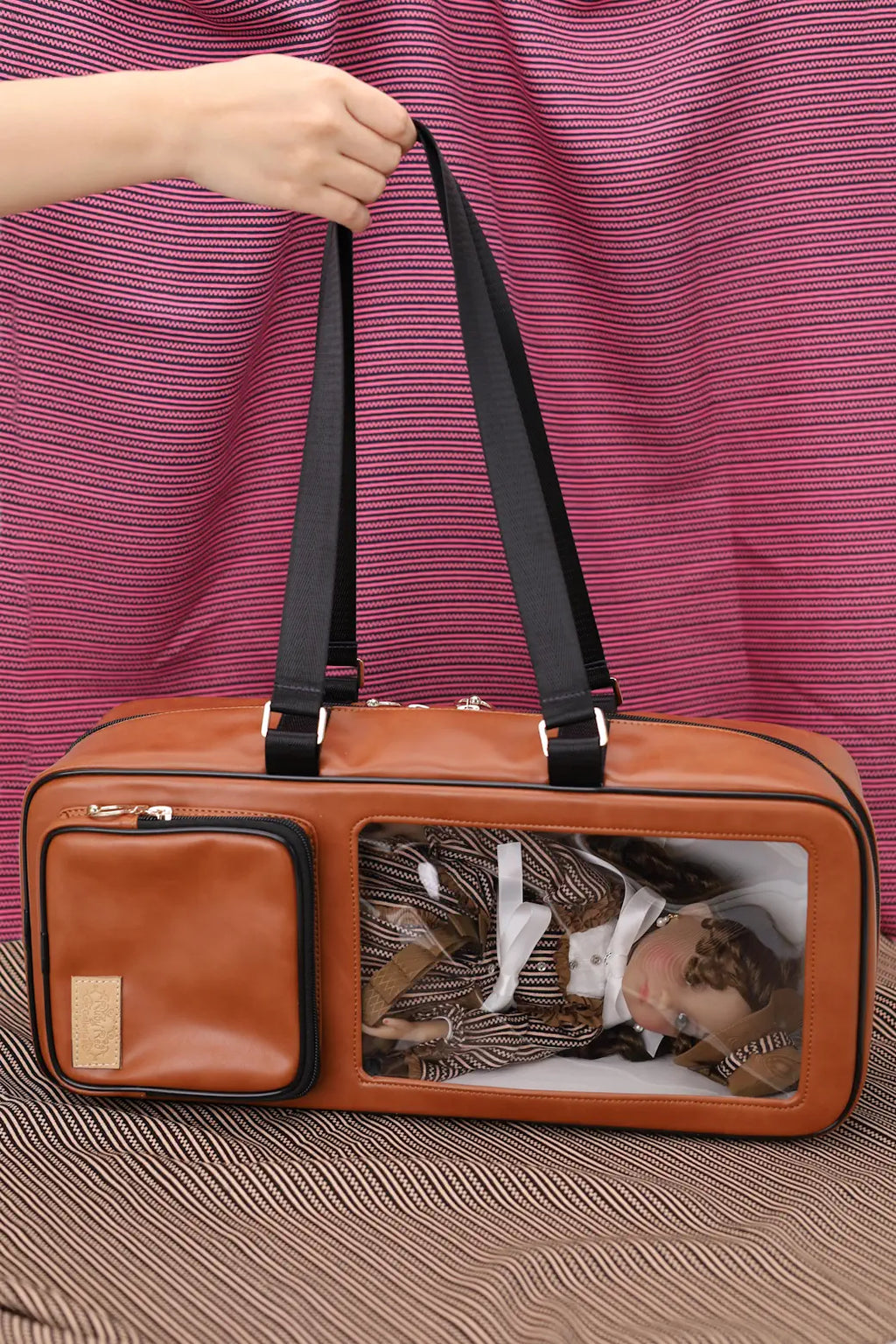 Brown pet carrier with a black handle against a striped purple and brown background