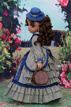 Doll in a vintage outfit with a blue hat and dress, holding a bag, against a floral background.