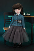 Doll in a Green jacket and gray skirt sitting on a chair with a dark background
