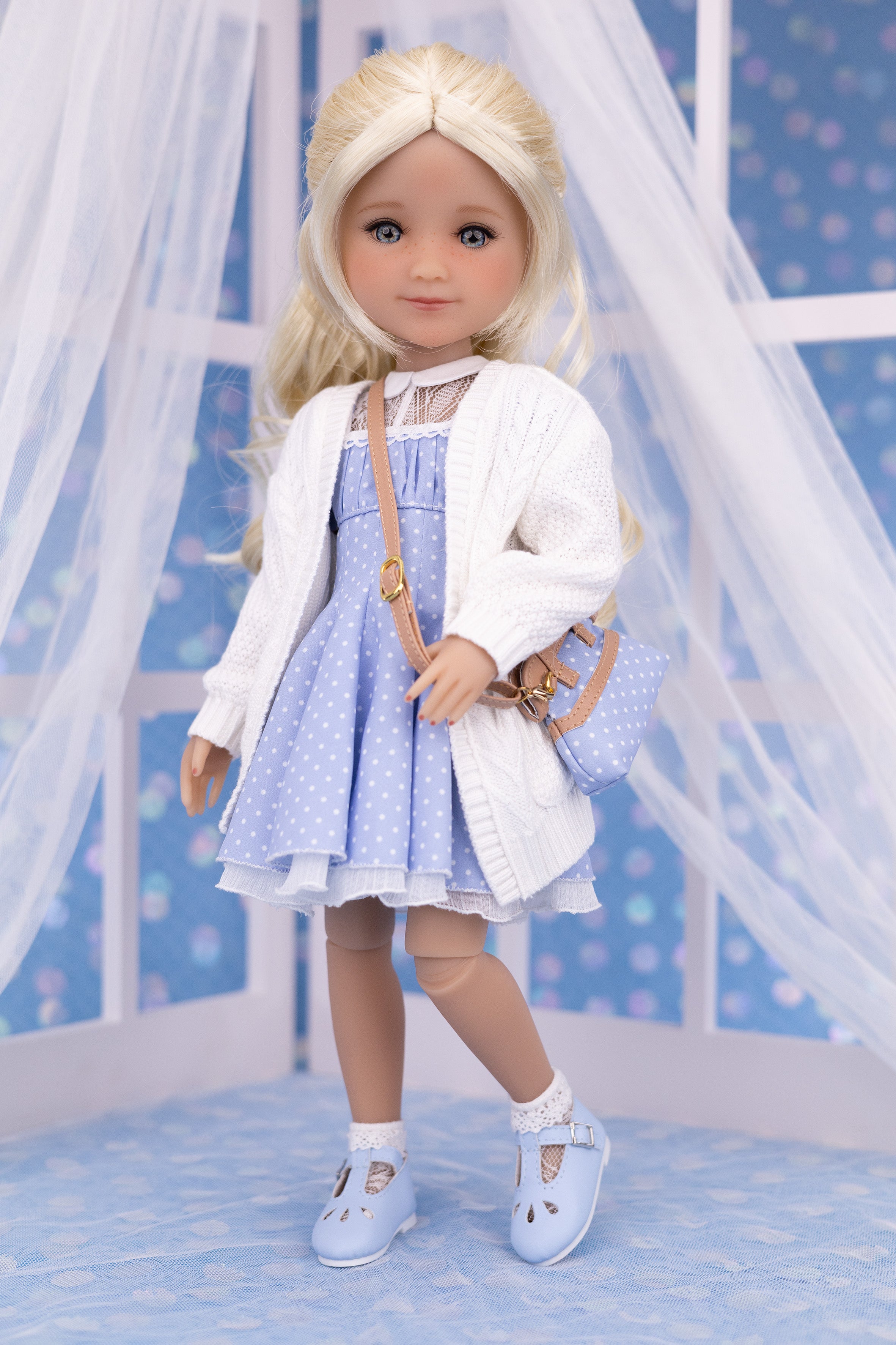 Doll wearing a white cardigan, blue dress, and white shoes with a blue background