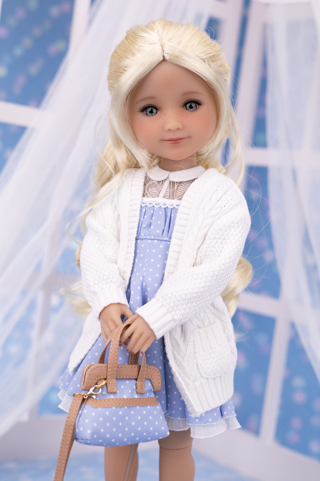 Doll wearing a white cardigan over a blue dress with a matching handbag against a light blue background.