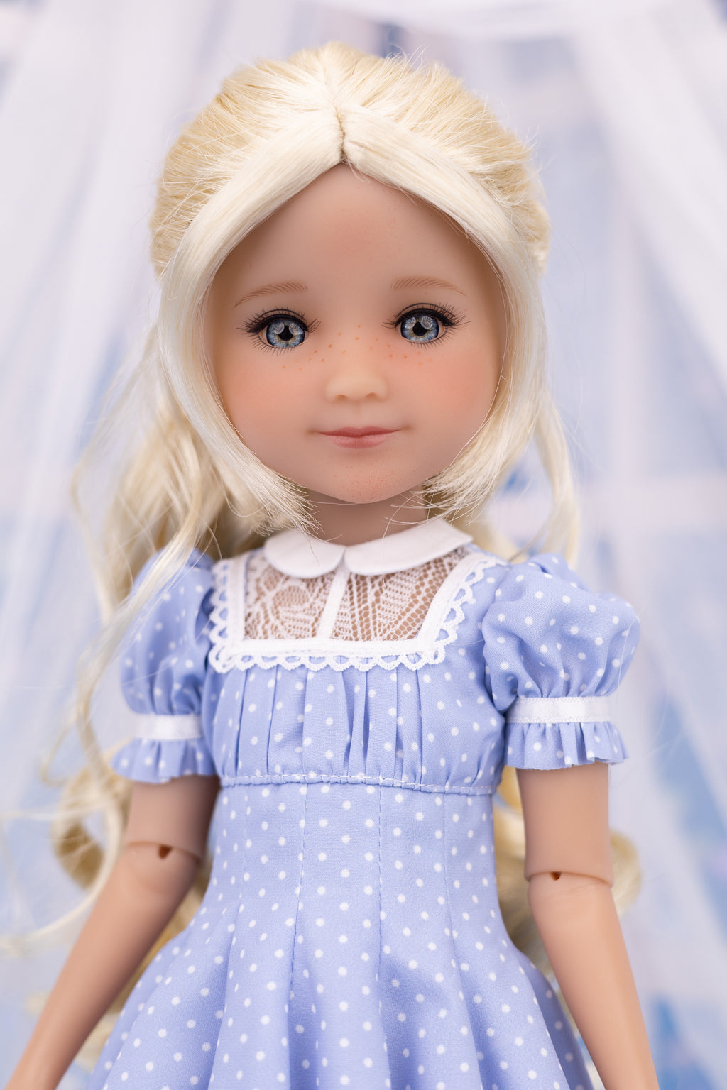 Doll with blonde hair wearing a blue dress with white polka dots and lace collar against a light blue background.