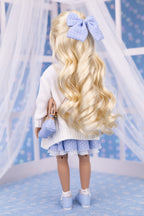 Doll with long blonde hair and a blue bow, wearing a white sweater and blue skirt, against a light blue background.