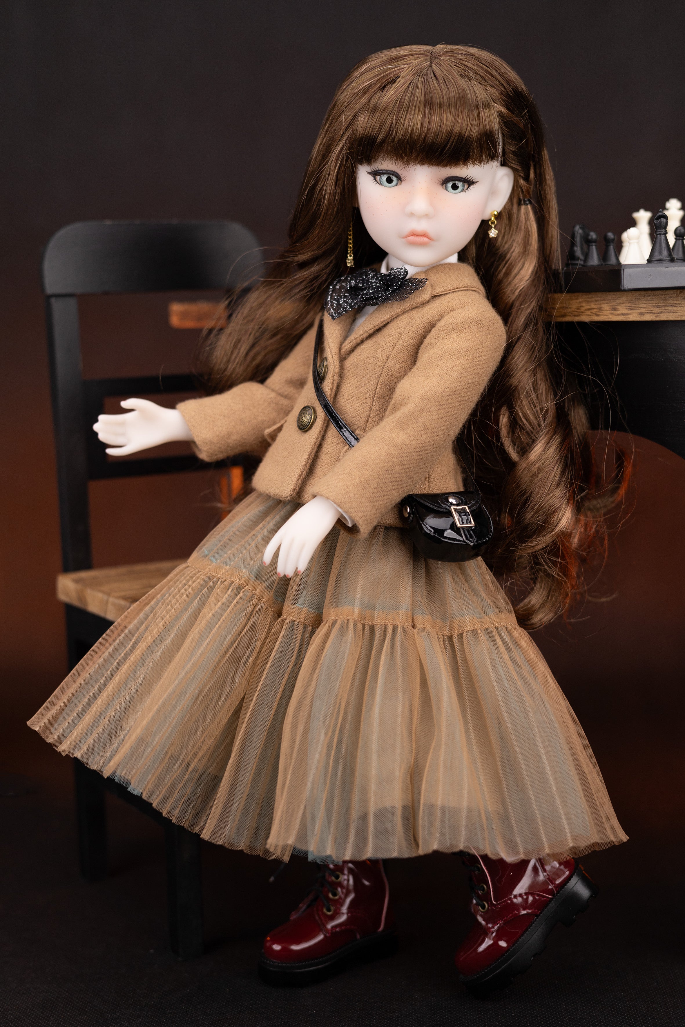 Doll in a brown coat and dress sitting on a chair with a dark background